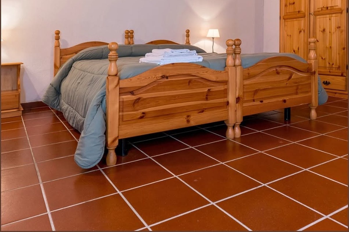 Camera dell'Agriturismo Abbatia con letti in pino accostati, piumone grigio-azzurro, asciugamani bianchi e pavimento in cotto